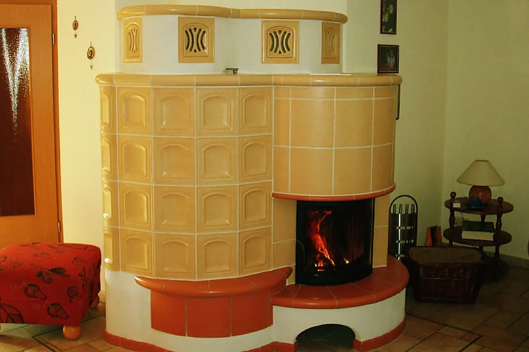 Großer Kachelofen mit quadratischen Kacheln, Holzscheiten und Feuer